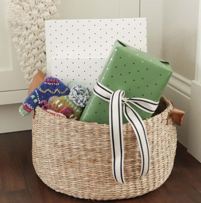 Basket with leather handles holding wrapped Christmas presents and fuzzy Anthropologie ornaments.