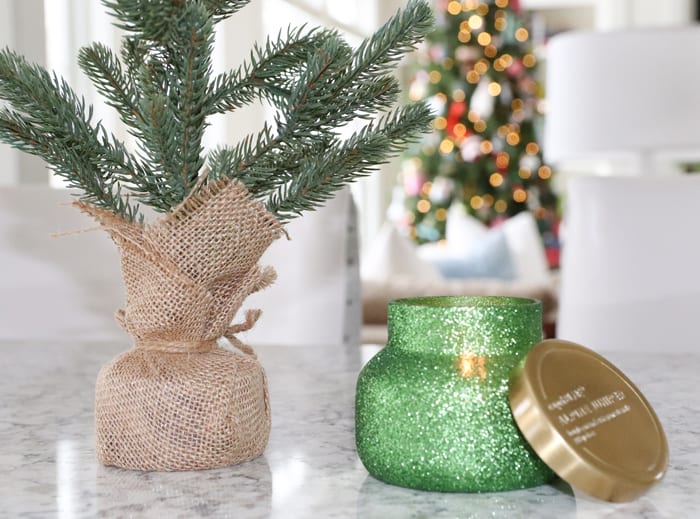 Capri blue green glitter Alpine Juniper candle with Christmas tree lights twinkling in the background.