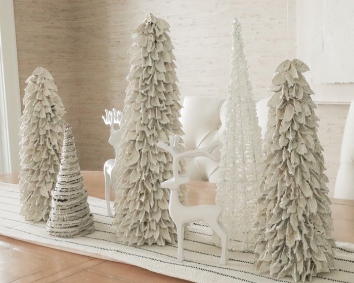 White wooden Christmas tree figurines and white reindeer figurines on dining room table centerpiece.