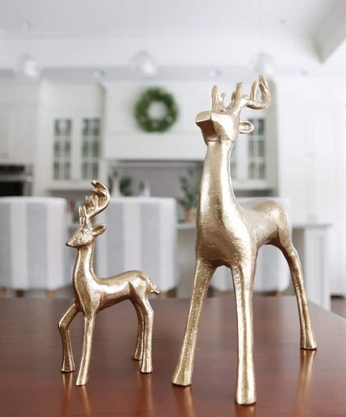 Gold reindeer figurines with a white kitchen and Christmas wreath blurred in the background.