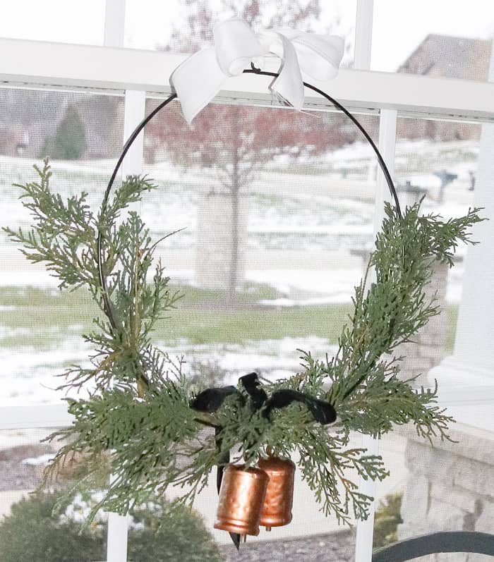 Magnolia Hearth and Hand wreath with black velvet bow and sleigh bells. Hanging from window by a white ribbon.