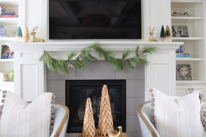 Faux garland hanging on fireplace mantel with colorful bottlebrush trees.