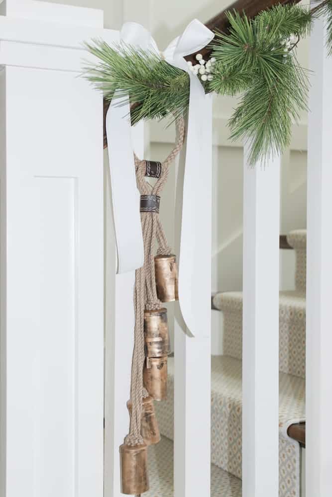 Close up of faux garland, white ribbon, and sleigh bells on stair railing.
