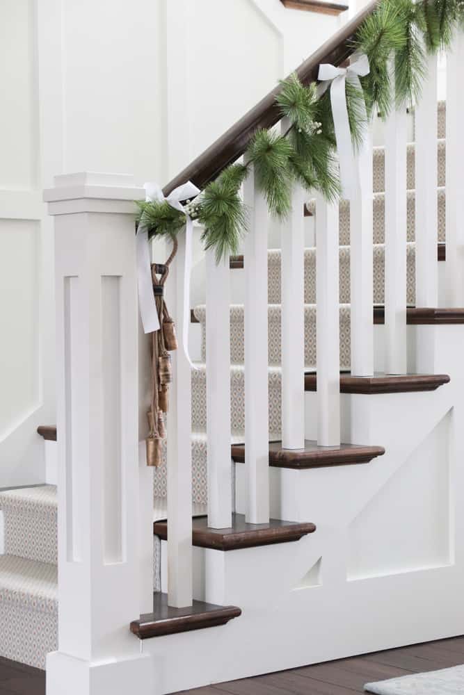Faux garland with white ribbon and sleigh bells on stairs with beautiful wainscoting.