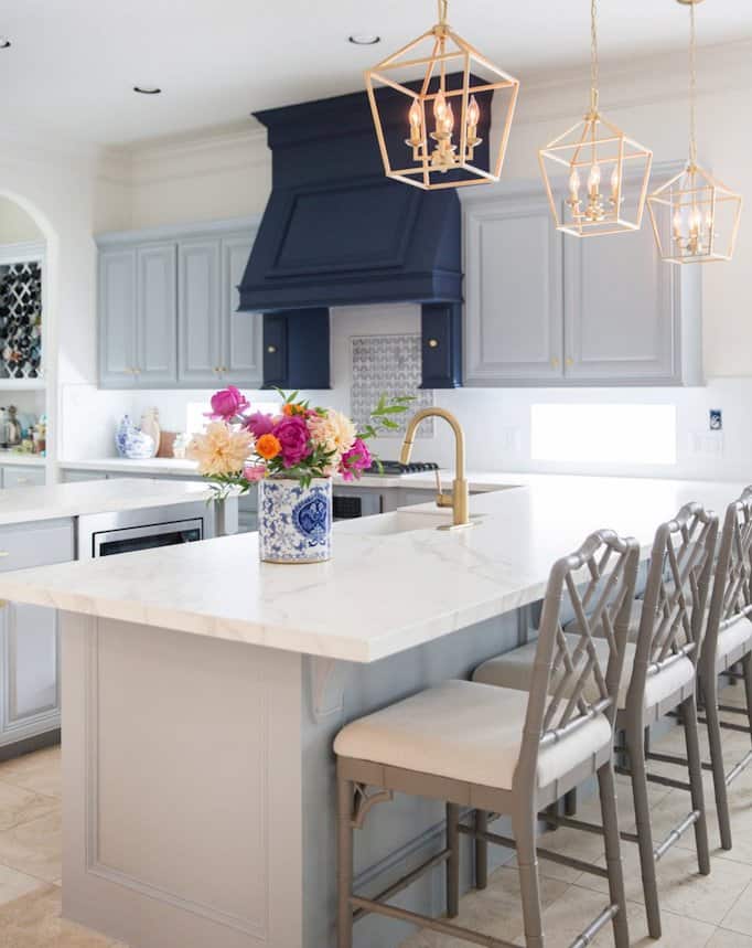 Light grey kitchen cabinets with white porcelain countertops and gold light fixtures