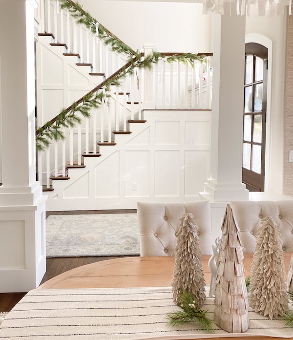 dining room christmas table with neutral decor and stairs in the background with faux garland