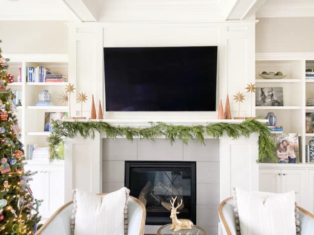 faux garland mcgee and co on mantle with wood tree figurines and gold starburts flanking tv